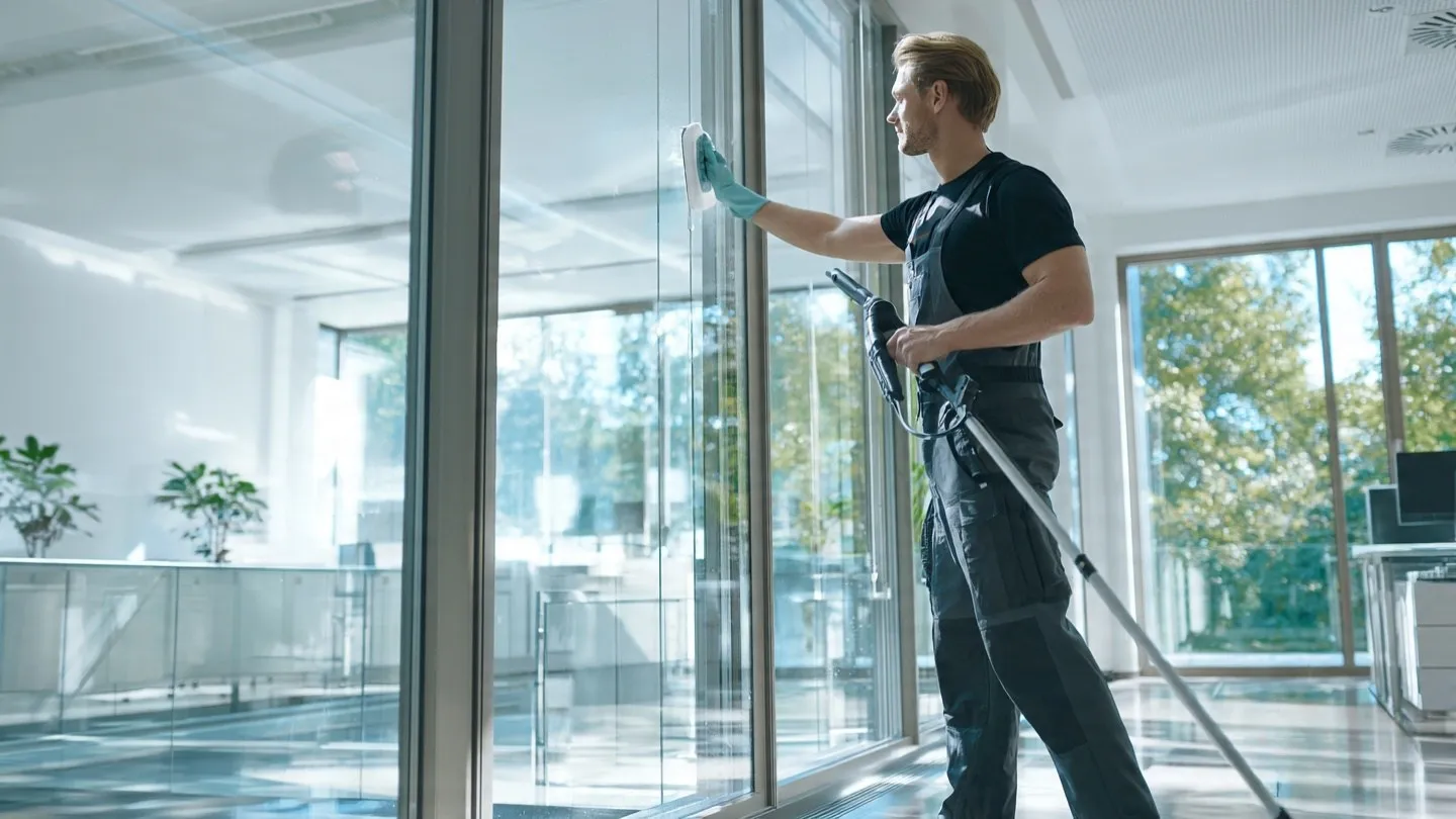 Fensterreinigung Firma München: Ein Mann reinigt die große Fensterwand eines Office-Gebäudes und sorgt für streifenfreie, klare Glasflächen.
