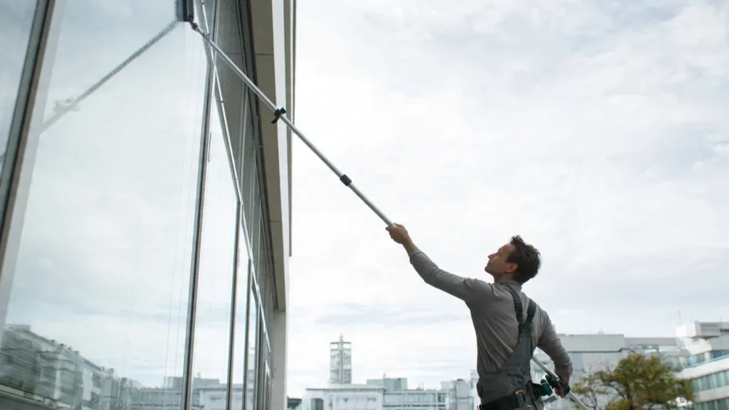 Professionelle Fensterreinigung München: Ein Mann reinigt die äußere Fensterfront eines Gebäudes und sorgt für streifenfreie, klare Glasflächen.